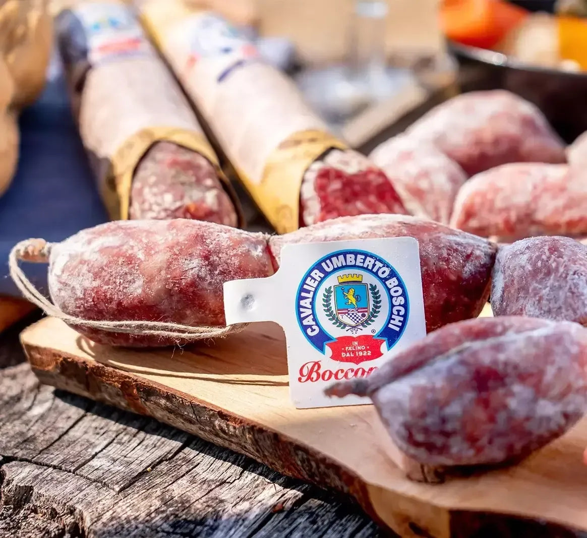Squisite fette di salame artigianale Cavalier Umberto Boschi, posate su un tagliere rustico, immerse in un ambiente naturale e accogliente.