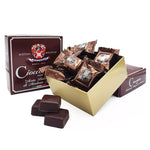 Eleganti cioccolatini ripieni di aceto balsamico, avvolti in carta dorata, presentati in una scatola con alcuni cubetti esposti, simbolo di gusto raffinato.