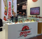 Uno stand Ortolina Classica vivace ed accogliente in fiera, esibendo prodotti vari e un logo di un pomodoro gigante.