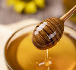 Un cucchiaio di legno raccoglie del miele di acacia dorato e lucente, pronto a deliziare il palato con la sua dolcezza naturale e vellutata.