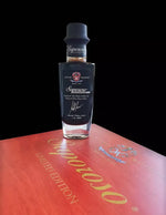 Un'elegante bottiglia di Aceto Balsamico di Modena, edizione Anniversario Saporoso limitata, presentata in un cofanetto rosso.