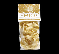 Una confezione di pappardelle biologiche all'uovo, fatte con semola di grano duro secondo la tradizione toscana, posata su un'elegante base nera.