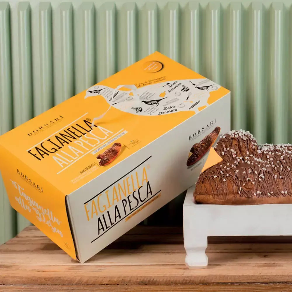 La Fagianella® presenta una confezione regalo in tonalità pesca, elegantemente posata accanto ad un dolce lievitato glassato, presentato su una raffinata alzatina bianca.