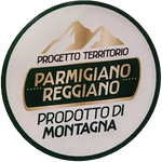 Un Parmigiano Reggiano DOP stagionato 24 mesi, presentato in mezza forma, si staglia tra un pittoresco scenario di montagne. Accanto, tre coltellini per il taglio artistico.