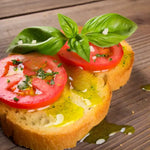 Una fetta di pane croccante accoglie pomodoro fresco e foglie di basilico, il tutto bagnato con l'olio extra vergine di oliva Monocultivar Taggiasca.