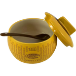 Una formaggiera color parmigiano, decorata e realizzata in ceramica, con un coperchio e un cucchiaio marrone, ideale per servire i formaggi.