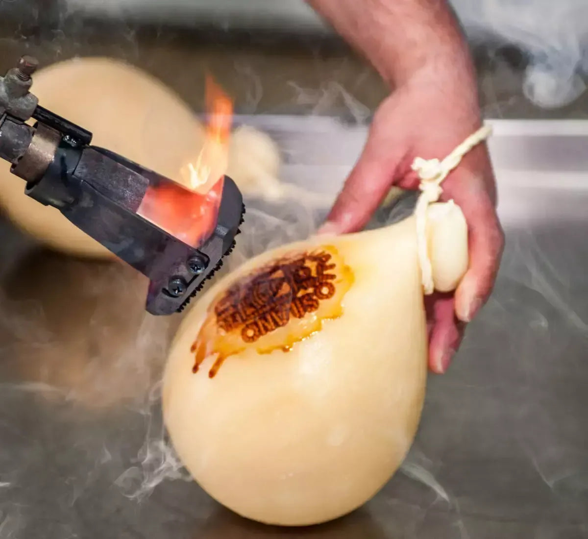 Una mano artigiana marca con fuoco vivo un Caciocavallo Silano DOP semistagionato, incarnando una tradizione secolare.