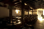 Un'antica cantina ospita botti di legno, illuminate da luce soffusa, per l'aceto balsamico tradizionale. Il profumo intenso evoca la tradizione.