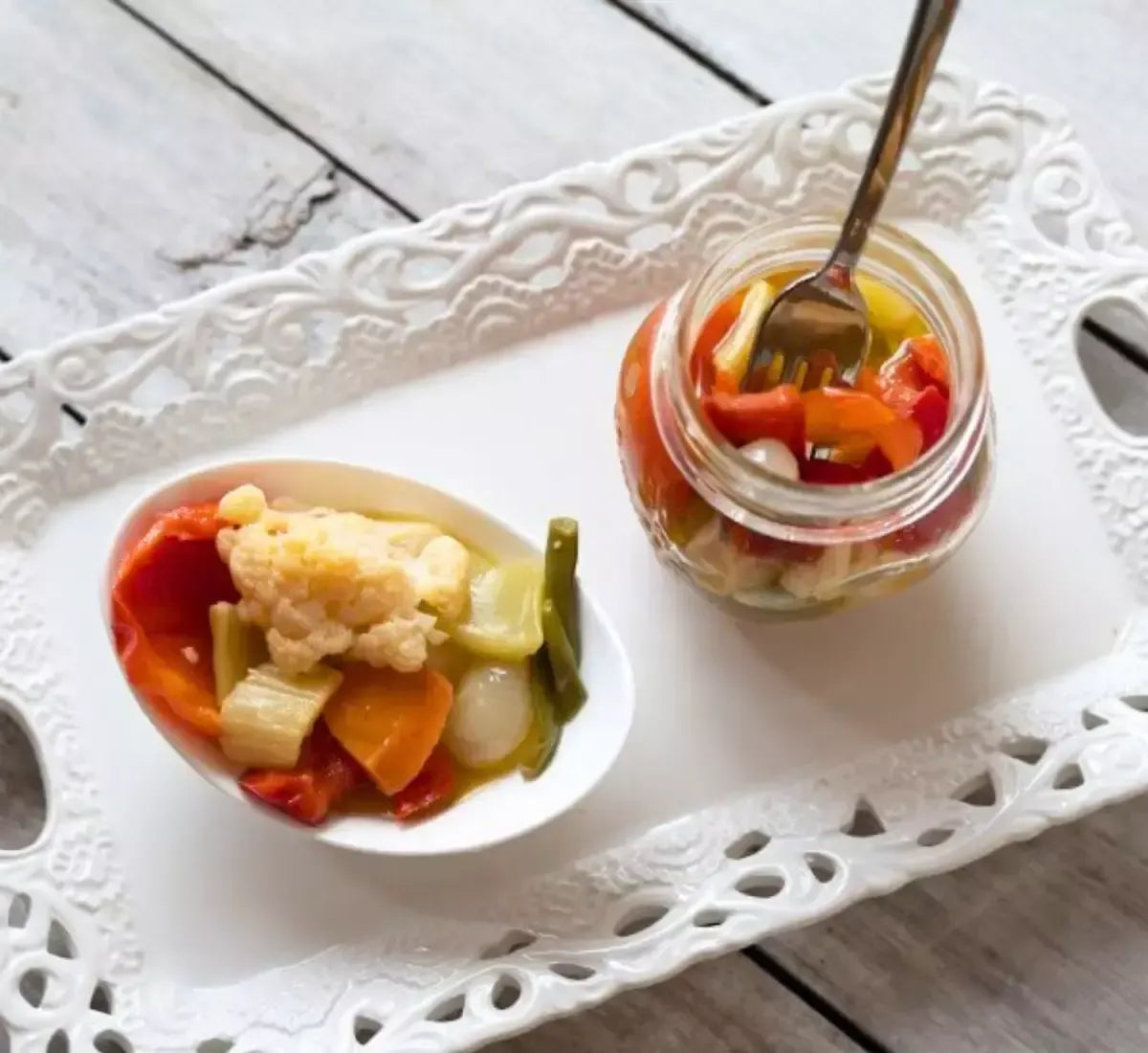 Un piatto bianco elegante ospita una giardiniera di verdure artigianali in agrodolce, accanto a un barattolo aperto e una forchetta pronta all'uso.
