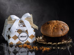 Un panettone dorato, arricchito da frutta candita, è avvolto con cura in un incarto artigianale ed elegante, posato su un piatto decorativo, esprimendo un'atmosfera festiva e sofisticata.