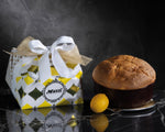 Un panettone al limoncello, avvolto a mano e adornato con un fiocco dorato, accanto a un limone, il tutto presentato in un packaging elegante su uno sfondo scuro e sofisticato.
