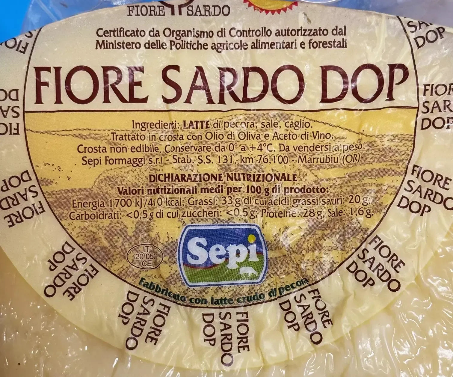 Un formaggio Fiore Sardo DOP stagionato, con crosta naturale, l'etichetta ne conferma gli ingredienti e l'origine certificata.
