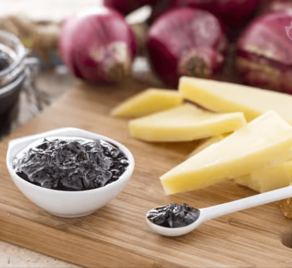 La mostarda di cipolle rosse, servita in una ciotola, accompagna formaggi su un tagliere, richiamando i gusti agrodolci dell'autunno.