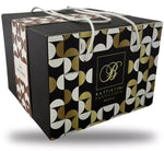 Un lussuoso panettone ai tre cioccolati presentato in una scatola regalo raffinata, adornata con un motivo geometrico e manici di corda.