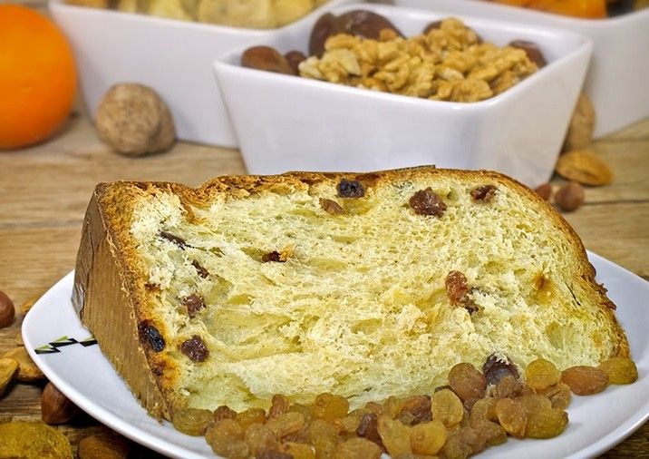Una fetta di panettone biologico, con uvetta e noci, è elegantemente disposta su un piatto, su un tavolo rustico.