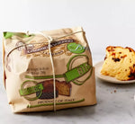 Un panettone biologico tradizionale, avvolto a mano con un nastro, posato su un tavolo di marmo. Accanto, una fetta dorata e frutta candita servita sul piatto.