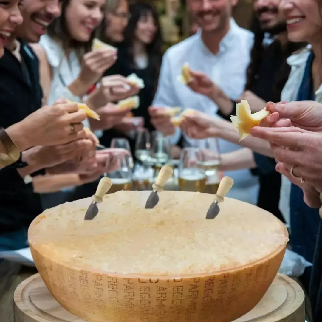 Un gruppo di amici si diverte a condividere un grande pezzo di Parmigiano Reggiano DOP di montagna, utilizzando tre piccoli coltelli.
