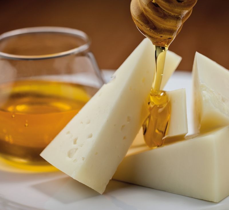 Fette bianche del gustoso Pecorino Toscano DOP stagionato, accompagnate da miele dorato che cola, creando l'abbinamento perfetto.