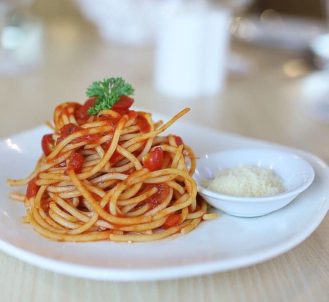 Spaghetti succulenti al pomodoro, arricchiti da prezzemolo fresco, serviti accanto a una ciotola di cremoso parmigiano Parmissimo grattugiato.