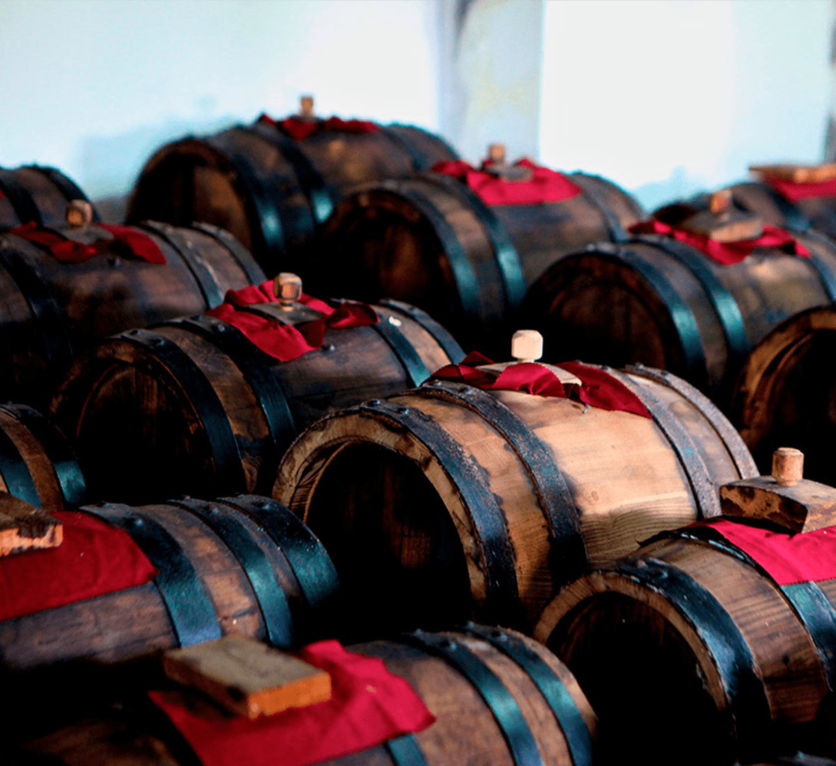 Antiche botti di legno, avvolte in panni rossi, custodiscono l'aceto balsamico tradizionale di Modena DOP invecchiato, in un'atmosfera autentica.