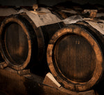 Antiche tradizioni evocate da botti di legno scuro per aceto balsamico tradizionale di Modena, sotto una luce soffusa.