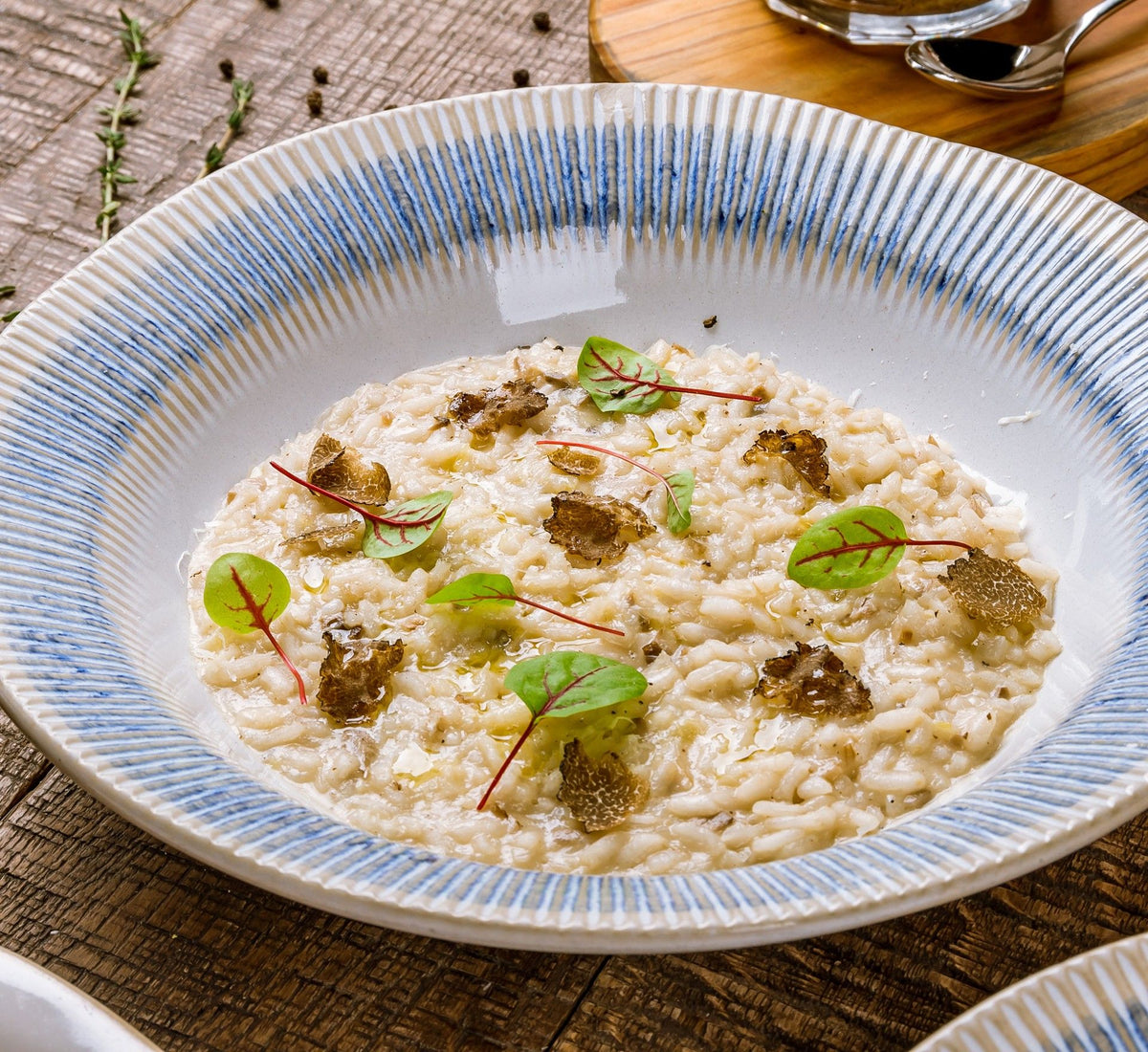En kremet og deilig risotto med trøffel, servert på en hvit tallerken med blå kanter, beriket med friske blader og et snev av pepper, presentert på et bord i rustikk stil.