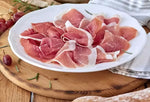 Su un piatto rustico, si adagiano fette di Prosciutto di Parma DOP stagionato 24 mesi, accanto a grappoli d'uva e rosmarino.