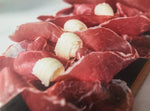 Fette di Culatello di Zibello DOP, stagionato 12 mesi, dall'intenso colore rosso, arricciate e accompagnate da riccioli di burro, presentate su un rustico tagliere.
