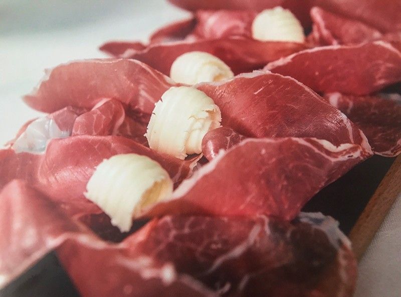 Fette di Culatello di Zibello DOP, stagionato 12 mesi, dall'intenso colore rosso, arricciate e accompagnate da riccioli di burro, presentate su un rustico tagliere.