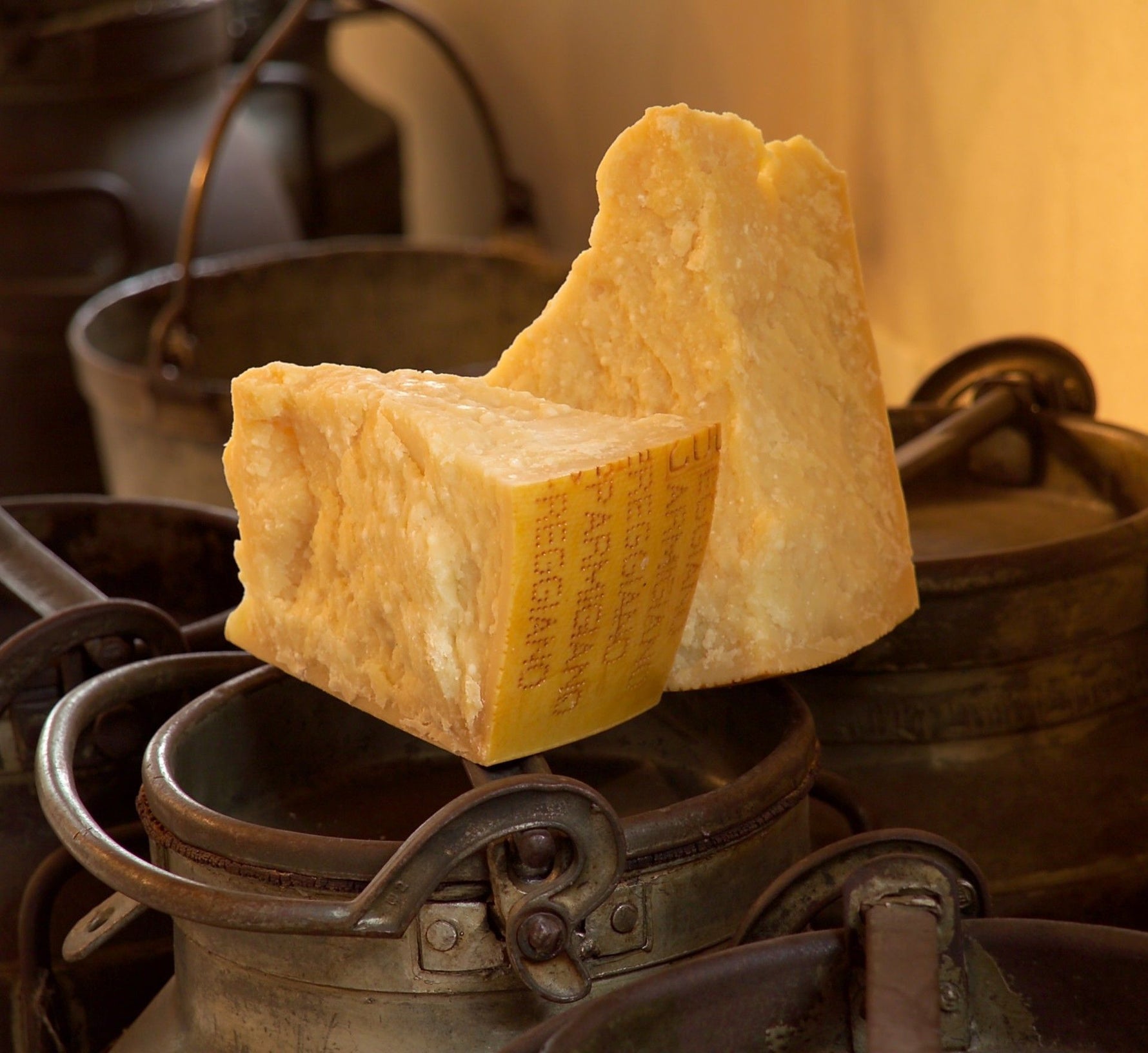 Un pezzo di Parmigiano Reggiano stagionato per 36 mesi, con una texture granulosa, posato su un autentico sfondo rustico di pentole di rame antiche.