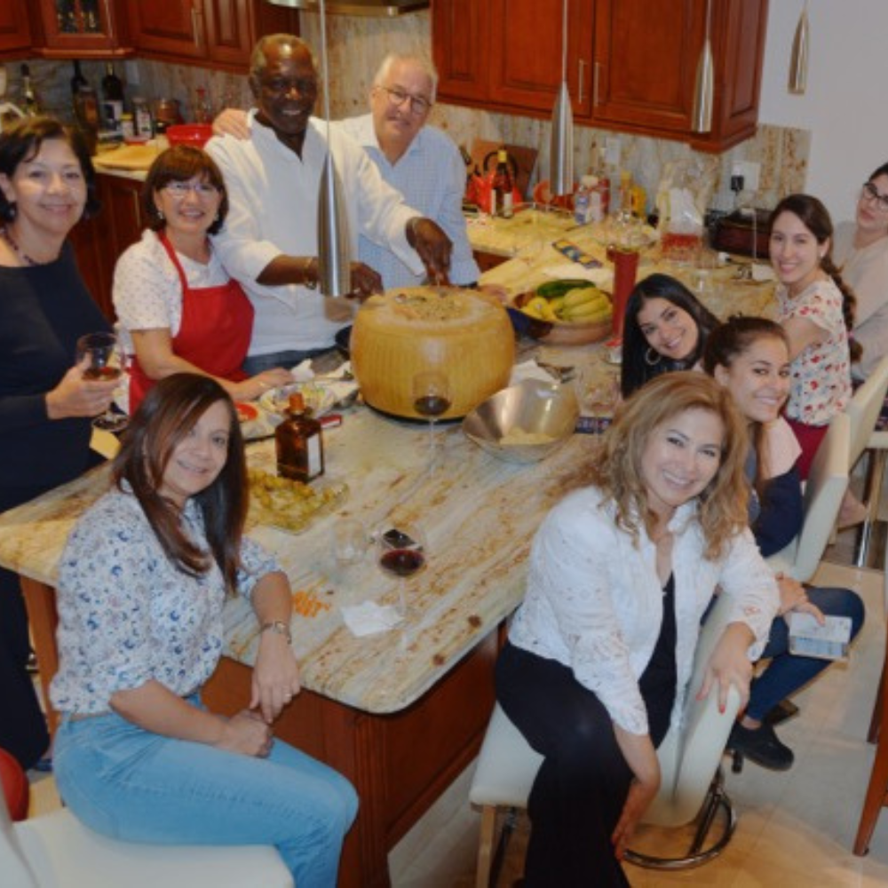 Gruppo di persone sorridenti attorno a un tavolo in una cucina accogliente con cibo e bevande, simbolo di convivialità.