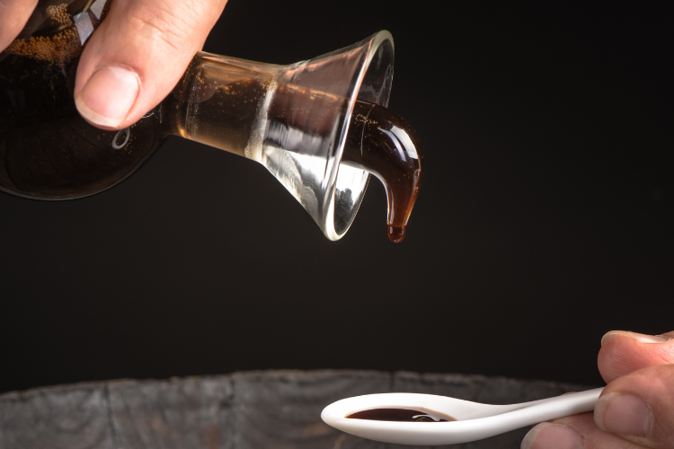 Versare aceto balsamico scuro in un cucchiaio bianco, momento di raffinata degustazione.