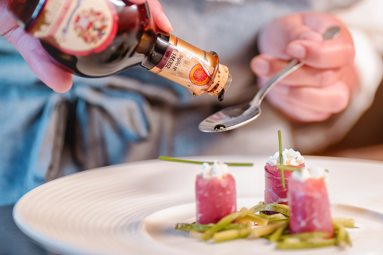 Delizioso aceto balsamico di Modena, versato su un cucchiaio per insaporire un piatto gourmet di alto livello.