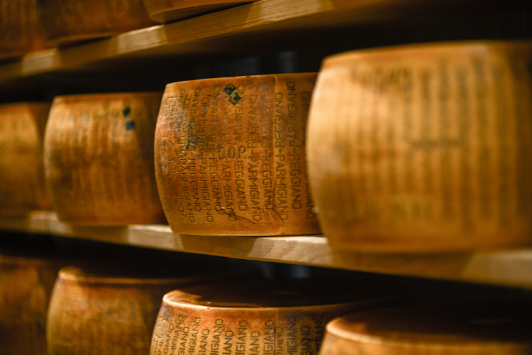 Forme di Parmigiano-Reggiano stagionato su scaffali di legno in una cantina tradizionale.