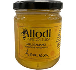 Un vasetto di miele artigianale italiano, dal colore dorato dell'Acacia, è adornato con un'etichetta elegante e un tappo nero. La sua presenza è delicata ed elegante.