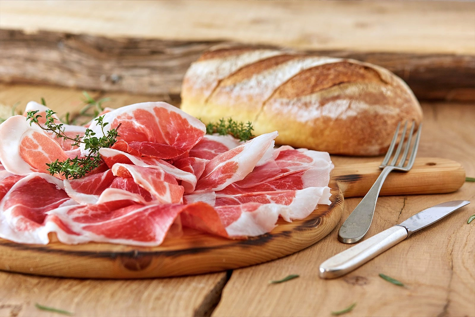 Fette di prosciutto DOP su tagliere rustico con pane e timo, risaltano su tavolo di legno per un'esperienza gourmet autentica.