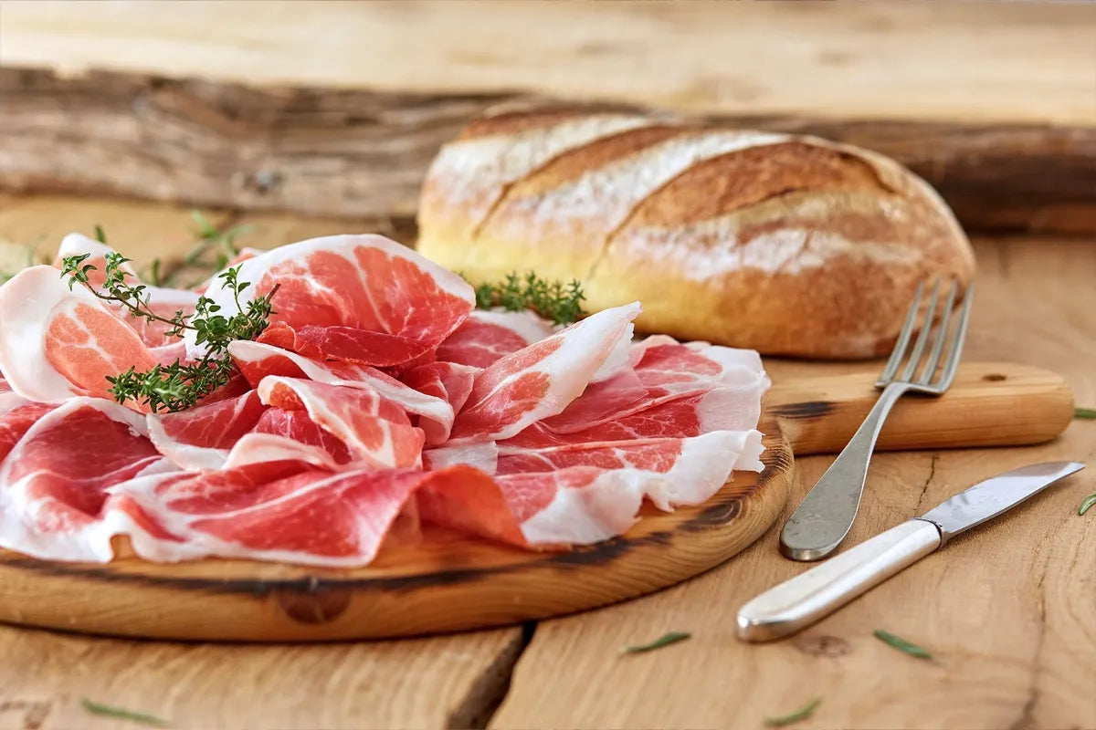 Fette di prosciutto DOP su tagliere rustico con pane e timo, risaltano su tavolo di legno per un'esperienza gourmet autentica.